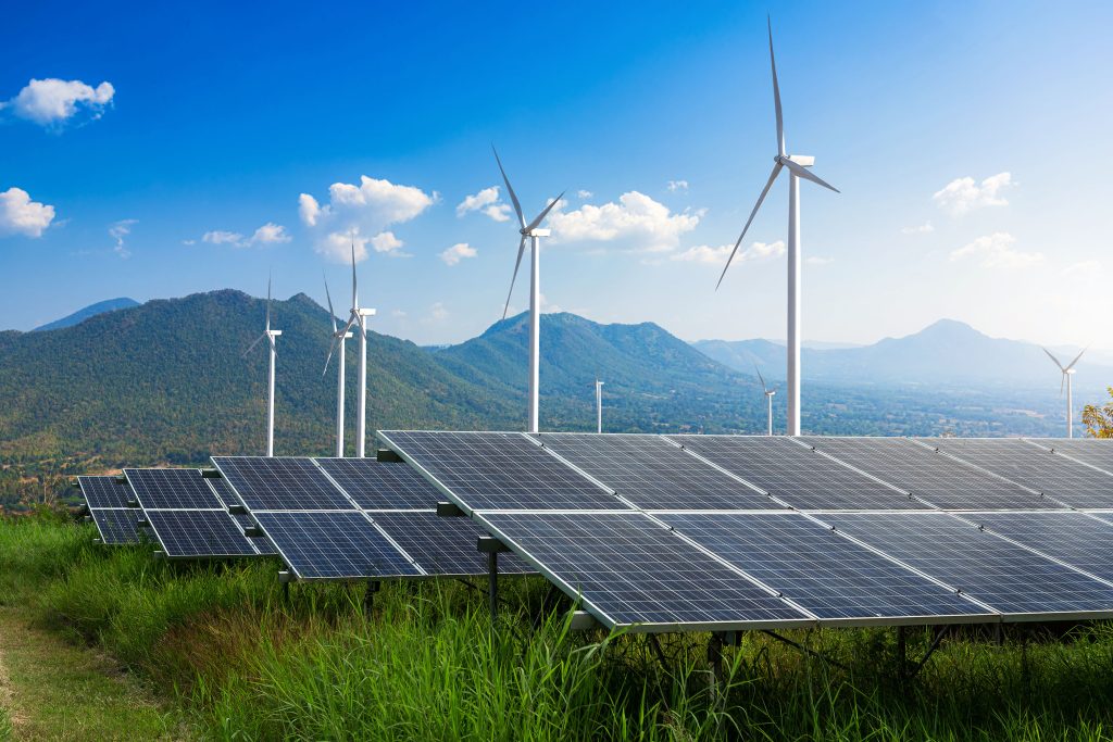 Photovoltaikmodule einer Solaranlage mit Windturbinen vor einer Berglandschaft unter blauem Himmel mit Wolken – Konzept für alternative Energie, saubere Energie, grüne Energie.