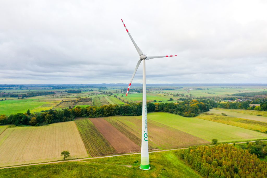 Windrad mit Respect Energy Logo in grüner Landschaft unter Wolkenhimmel.